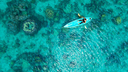 Aerial view of a woman and a young man kayaking on clear blue waters at Andaman Island. She does water sports activities.	