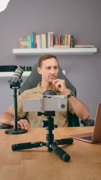 A podcaster is recording content in a home studio with a microphone and camera setup