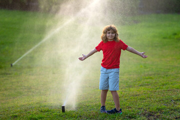 Kid play in garden near irrigation watering sprinkler system. Watering grass with automatic sprinkler. Lawn and gardening concept. Child backyard gardening. Child watering plants, watering sprinkler.