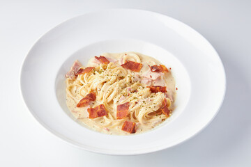 Spaghetti Carbonara topped with ham and bacon served in white plate isolated on white background....