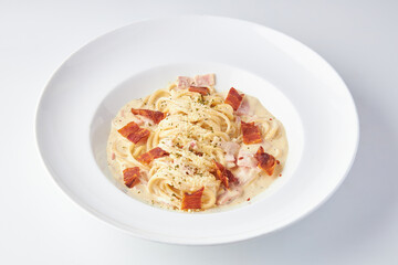 Spaghetti Carbonara topped with ham and bacon served in white plate isolated on white background....