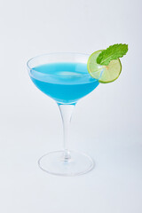 Blue Margarita cocktail in transparent glass decorated with sliced lime and mint leaves isolated on white background.