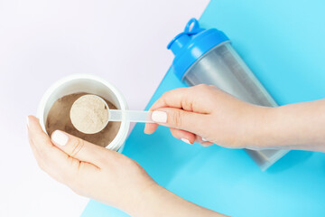 Female hand holding scoop with protein powder on blue and pink background top view.