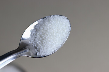 Close up of sugar in steel spoon with plain background.