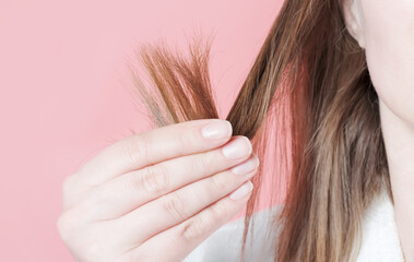Woman holding her hair with split ends close-up on pink background.