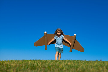Kid with toy jetpack outdoor. Child playing in green spring field with cardboard wings. Spring travel and adventure. Kids success and leader, startup concept.
