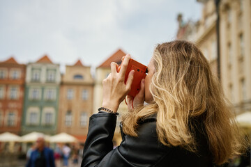 Woman taking picture using orange instant camera. Tourist captures memories during travel with...
