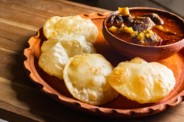 luchi or puri and mutton curry or laal maas served on earthen plate. Luchi is indian flatbread made of flour and deep fried. traditional indian meal.