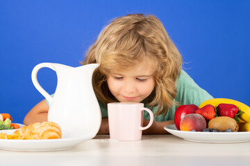 Child drink dairy milk. Cute kid drinking milk on blue studio background. Children eat breakfast.