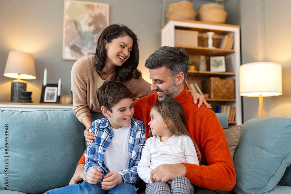 Poster Happy family having fun at home, parents and little children sit on sofa together, Happy family sitting on sofa laughing together. Cheerful parents playing with their kids at home.