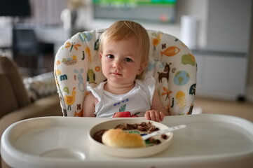 Adorable little girl sitting in high chair and eating