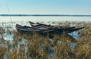 Pair of traditional wooden made fishing boats lying idly on grassland, submerged in shallow water of Damodar river embankment. Photo taken near Panchet Dam, in Purulia.