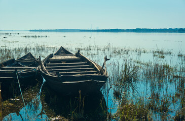 Fototapeta premium Pair of traditional wooden made fishing boats lying idly on grassland, submerged in shallow water of Damodar river embankment. Photo taken near Panchet Dam, in Purulia.
