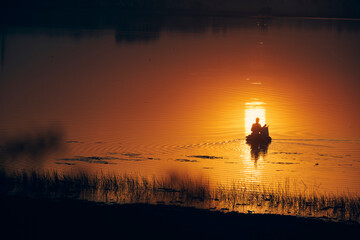 majestic evening view at Baranti lake (a popular travel spot in Purulia), with holden hued last rays of setting sun creating a magical backdrop. A lone person on floating raft seen fishing in water.