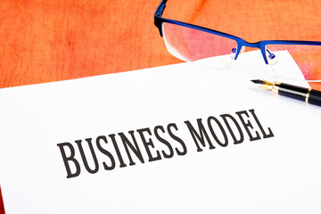 BUSINESS MODEL text an inscription on a white sheet on the table near glasses and a fountain pen
