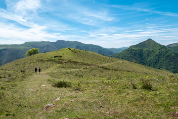 Montanha de Artzamendi num dia de primavera com verdes pastagens e dois turistas a caminharem ao fundo no País Basco em França