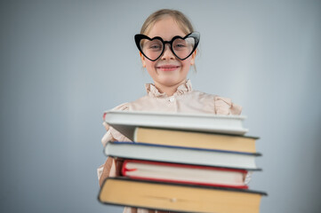 Little girl with glasses holding a stack of books on a white background. 