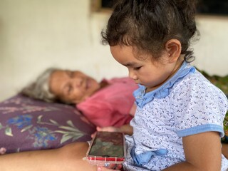 Asian girl with mobile phone sitting next to great-grandfather