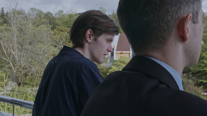 Two young men standing on balcony and communicating. Stock clip. Business partners discussion and green spring vegetating on the background.