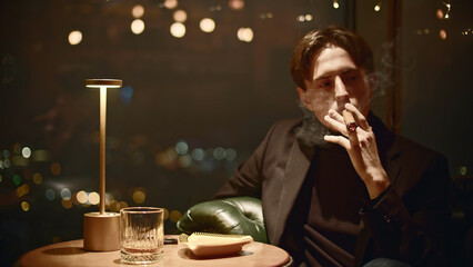 Young man smokes cigar in restaurant. Media. Elegant man in suit smokes cigar in restaurant. Mafia...