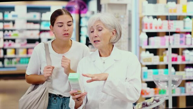 Polite old female pharmacist consulting young girl about care product in box in chemist's shop. High quality 4k footage