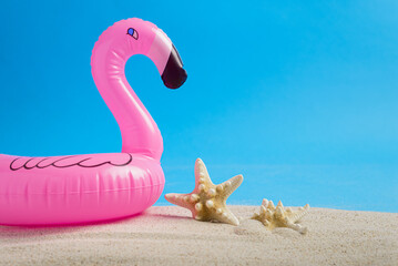 Starfish skeletons next to flamingo shaped lifeguard on beach sand with blue background. Summer...