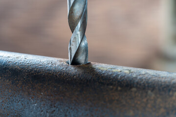 Metal drill bit make holes in pipe on industrial drilling machine, closeup. Metal work industry