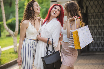 A group of girls walks down the street with packages after shopping. Three girlfriends are shopping along the street in the summer with packages and bags. Plus size girl with red hair
