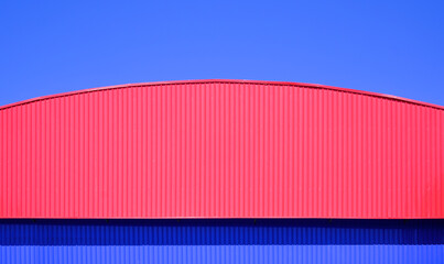 Red aluminium dome roof with blue corrugated steel wall of colorful industrial warehouse building...