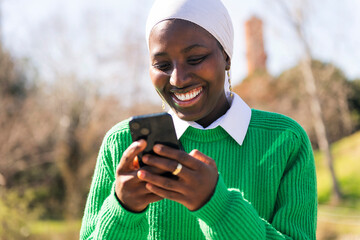 young african woman smiling happy using mobile phone outdoors, concept of technology of...