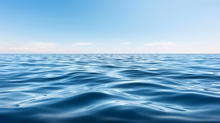 Obraz premium A vast expanse of blue water, topped with a clear sky bearing scattered clouds, descends into undulating waves below
