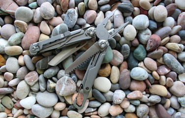 Half-opened full metal multi-tool with different blades and folding screwdrivers on colored pebbles
