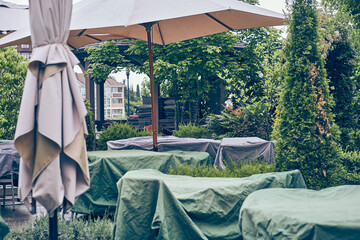 Summer cafes are covered with covers in an empty outdoor cafe. Tables and chairs are closed at...