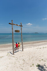 Two little children sitting on a swing on the beach