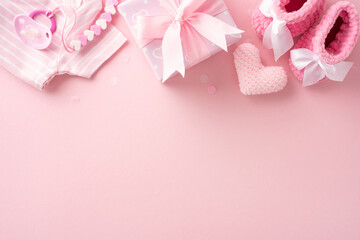 Flat lay image of pink baby shower decorations with baby clothes, pacifier, and gift box on a pink background