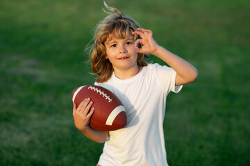 Kid boy playing with rugby ball in park. Cute child having fun and playing american football on green grass park.