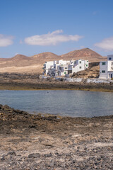 Bay and typical houses of the fishing village of Caleta de Caballo. White houses. Rock coast in the foreground. Turquoise water. Calm sea. Caleta de Caballo, Lanzarote, Canary Islands, Spain.