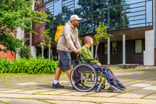 Man pushing happy university student in wheelchair along the campus