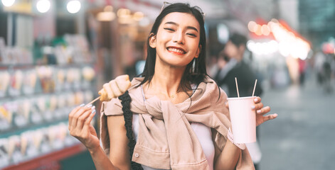 Happy asian foodie woman eating street food holding korea skewer oden