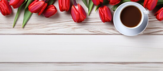 A flat lay of red tulips with a coffee cup placed on a white wooden table providing ample copy space in the image