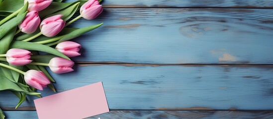 A Mother s Day concept featuring pink tulips and a postcard arranged on a blue wooden background A flat lay image with available copy space