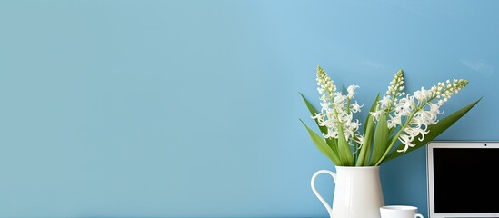 A work from home setup with a desk laptop coffee and a lovely bouquet of lily of the valley flowers The background is a calming blue creating a serene atmosphere Perfect for bloggers freelancers and
