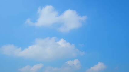 A clear blue sky with a few scattered, fluffy white clouds. The clouds are soft and billowy,...
