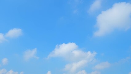 A bright blue sky with scattered, fluffy white clouds. The clouds have a soft, billowy appearance, creating a pleasant contrast against the clear blue background. The scene is serene and uplifting.
