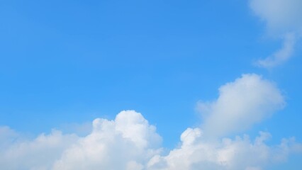 A bright blue sky with large, fluffy white clouds. The clouds have a soft, billowy appearance,...