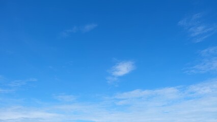 A clear blue sky with a few scattered white clouds. The sky transitions from a deeper blue at the top to a lighter blue near the horizon, creating a calm and peaceful atmosphere. Cloud background.
