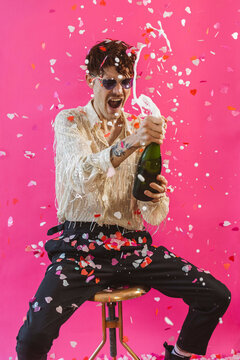 Cheerful non-binary person celebrating with champagne against pink background