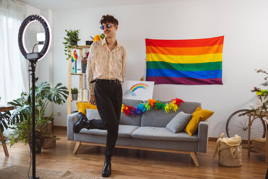 Smiling influencer vlogging with mobile phone in front of rainbow flag at home