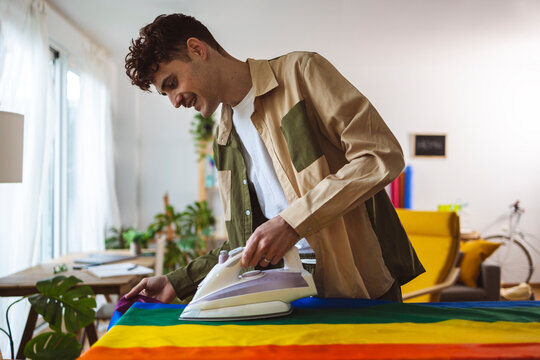 Smiling man ironing rainbow flag at home