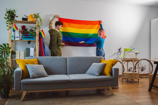 Friends hanging rainbow flag and preparing for pride party at home